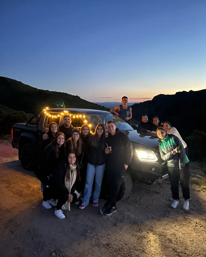 El grupo posa al anochecer junto a la camioneta, con lucecitas y mate.